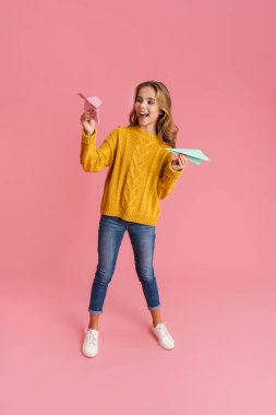 Neşeli güzel sarışın kız gülümsüyor ve pembe arka planda izole edilmiş kağıt uçaklar atıyor.