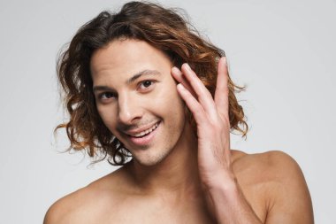 Mutlu gömleksiz adam gülümsüyor ve yüzüne dokunuyor. Beyaz arka planda soyutlanmış.