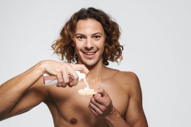 Beyaz arka planda izole edilmiş kozmetik sünger ve temizlik köpüğü kullanan mutlu üstsüz adam.