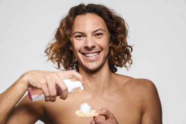 Kozmetik sünger ve temizlik köpüğü kullanan gülen adam beyaz arka planda izole edilmiş.