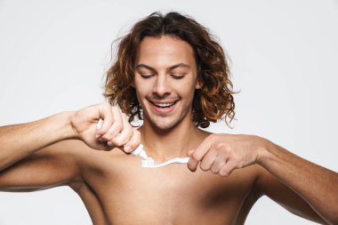 Beyaz arka planda dişlerini fırçalarken gülümseyen mutlu üstsüz adam.