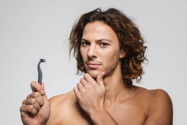 Beyaz arka planda jiletle poz veren ciddi, üstsüz, yakışıklı bir adam.