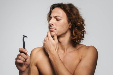 Beyaz arka planda jiletle poz veren ciddi, üstsüz, yakışıklı bir adam.