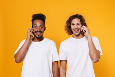 Sarı arka planda izole edilmiş cep telefonlarıyla konuşan iki mutlu gencin portresi