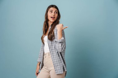 Heyecanlı güzel kız mavi arka planda izole edilmiş bir şekilde işaret ediyor.