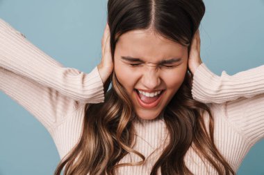 Heyecanlı güzel bir kız çığlık atıyor ve kafasını tutuyor. Mavi arka planda izole bir şekilde.