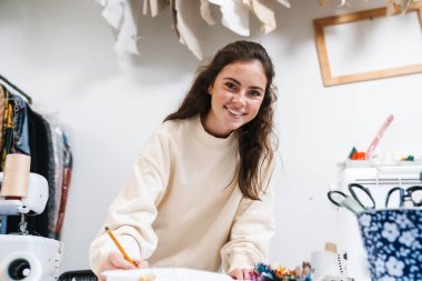 Atölyede çalışırken gülümseyen güzel, mutlu esmer bir terzi kız.