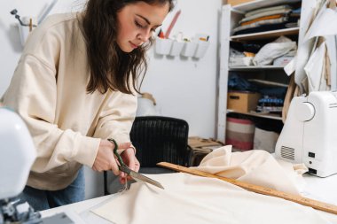 Atölyede çalışırken kumaş kesen esmer, güzel bir kız.