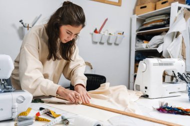 Atölyede kumaşla çalışan güzel esmer kız terzi.