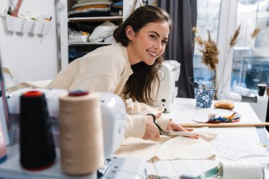 Atölyede çalışırken kumaş kesen güzel esmer kız.