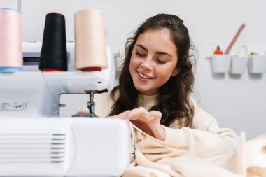 Atölyede dikiş makinesiyle çalışırken gülümseyen mutlu bir terzi kız.