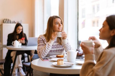 İki güzel gülümseyen genç bayan arkadaş kafeteryada oturmuş çay içerken yemek yiyorlar.