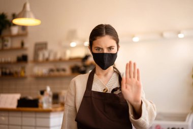 Ciddi genç barista müşterileri tıbbi maskesiz kahve dükkanına girmekten men ediyor.