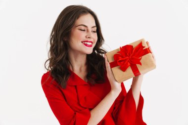 Kırmızı elbise giyen mutlu çekici kız beyaz arka planda izole edilmiş hediye kutusu gösteriyor.