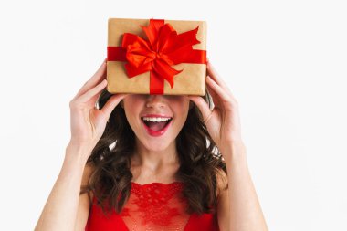 Kırmızı elbise giyen mutlu çekici kız beyaz arka planda saklanmış hediye kutusuyla dalga geçiyor.