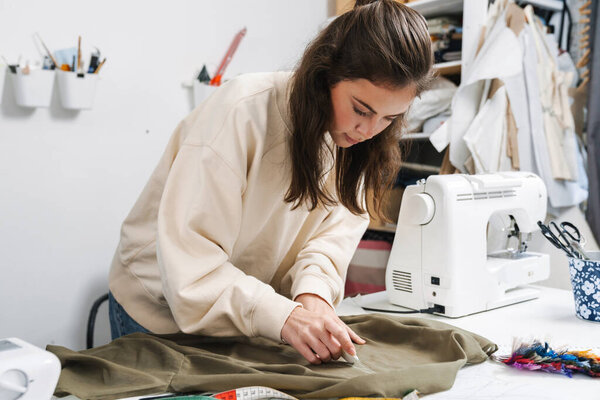 Focused nice brunette girl seamstress working with fabric in atelier