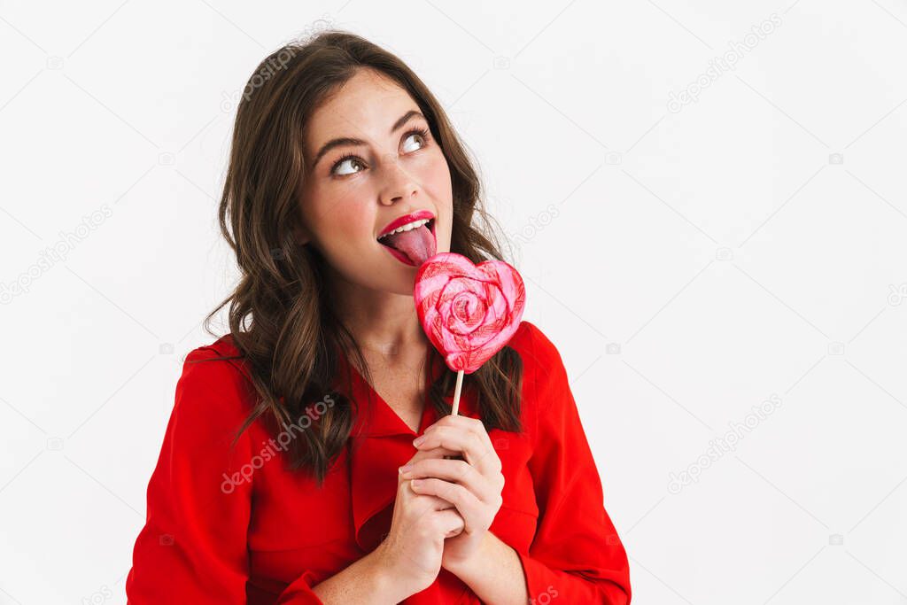 Dreaming beautiful girl wearing red dress liking lollipop isolated over white background