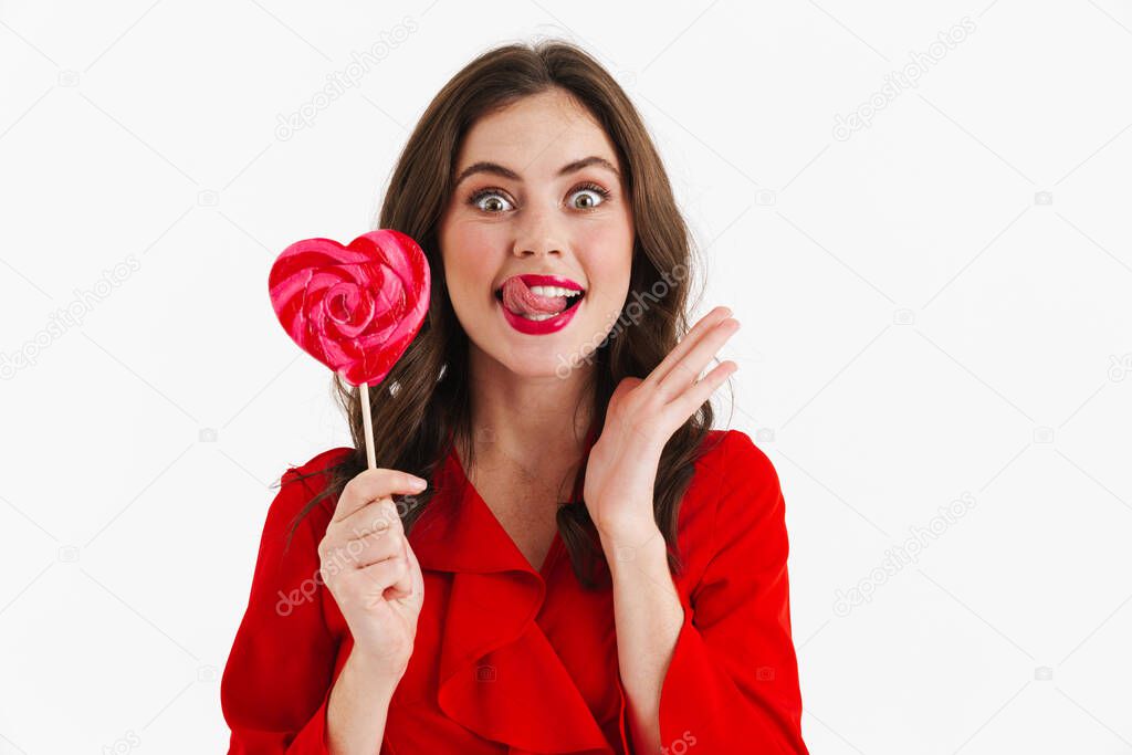 Excited beautiful girl showing her tongue while liking lollipop isolated over white background