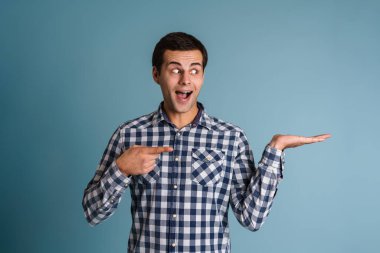 Mutlu heyecanlı genç adam sunar kopya alanı mavi arkaplan üzerinde izole