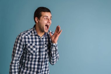 Heyecanlı genç beyaz adam mavi arka planda izole edilmiş bir şekilde bakıyor ve çığlık atıyor.