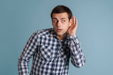 Odaklanmış genç esmer adam yana bakıyor ve mavi arka planda izole edilmiş kulak misafiri.