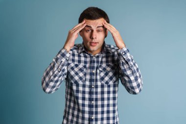 Kafası karışmış genç adam mavi arka planda izole edilmiş.