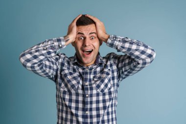 Mutlu, heyecanlı genç adam mavi arka planda izole edilmiş kameraya bakıyor.