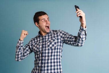 Mavi arka planda tek başına dikilirken selfie çeken mutlu genç adam.