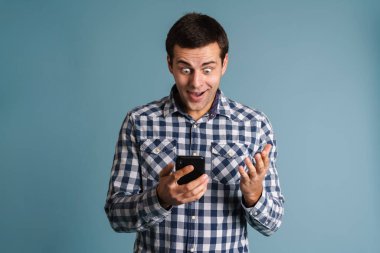 Mavi arka planda izole edilmiş cep telefonu kullanan yakışıklı genç adam.