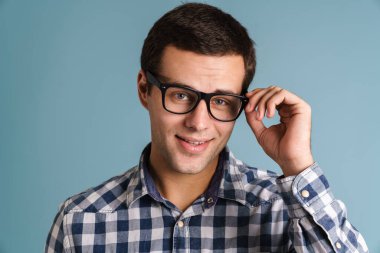 Mavi arka planda izole edilmiş, gözlüklü mutlu gülümseyen adam portresi.