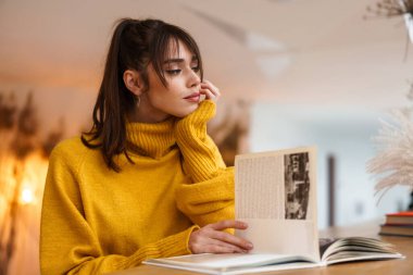 Kapalı bir kafede oturmuş kitap okuyan güzel, odaklanmış bir kız.