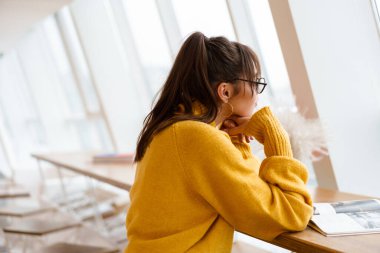 Kapalı bir kafede otururken gözlüklü güzel kız kitap okuyor.