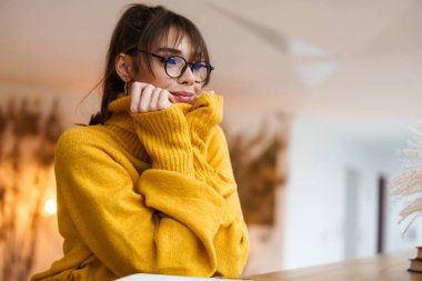 Kapalı bir kafede otururken gülümseyen gözlüklü güzel, neşeli kız.