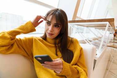 Çekici mutlu kız cep telefonu kullanıyor ve koltukta oturuyor.