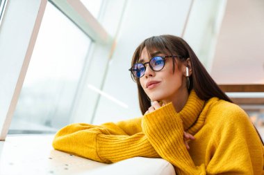 Büyüleyici gözlüklü kız kulaklıklı müzik dinliyor ve kanepede oturuyor.