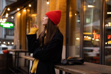 Şehir caddesinde dikilirken sigara içen şapkalı beyaz bir kız.