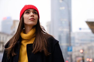 Beyaz şapkalı çekici kız şehir sokaklarında poz verirken yukarı bakıyor.