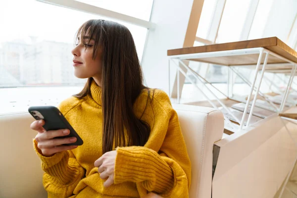 Çekici mutlu kız cep telefonu kullanıyor ve koltukta oturuyor.