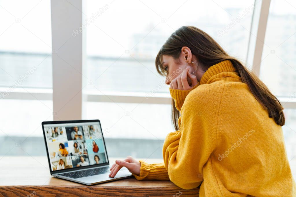 Charming serious girl working with laptop while sitting at table indoors