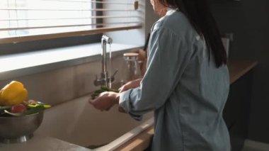 Güzel bir kadının arka manzarası mutfakta duran sebzeleri yıkıyor.