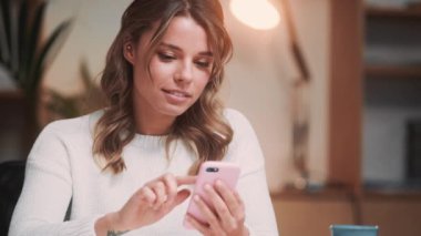 Güzel bir kadın akıllı telefonunu dairenin içinde otururken kullanıyor.