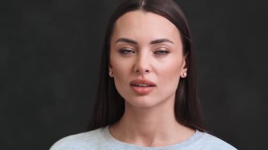 Sıkılmış genç bir kadının yakın plan görüntüsü başını yana çeviriyor. Stüdyodaki siyah bir arka planda tek başına duruyor.