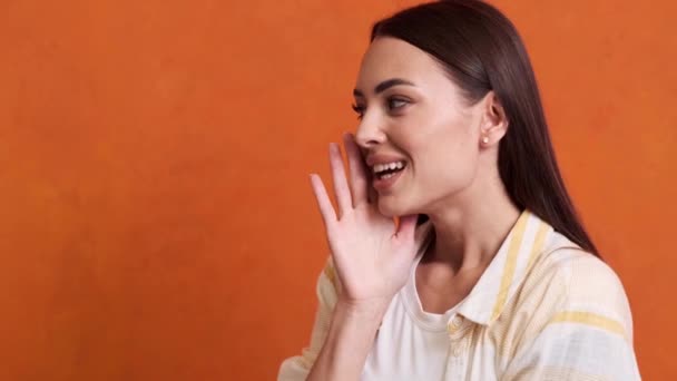 Una Joven Sonriente Está Compartiendo Secretos Aislados Sobre Fondo Naranja — Vídeos de Stock