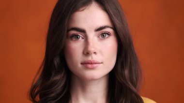 Güzel genç bir kadının yakın plan görüntüsü stüdyoda turuncu bir arka planda izole bir şekilde kameraya bakıyor.