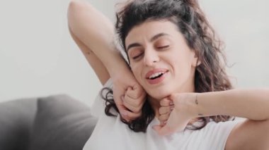 Gözleri kapalı gülümseyen genç bir kadın kollarını uzatıyor evdeki koltukta oturuyor.