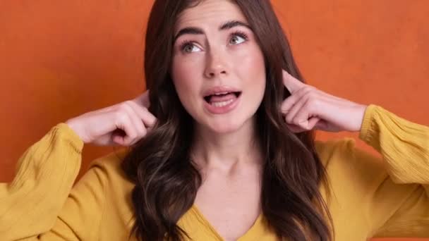 Недовольная Молодая Женщина Закрывает Уши Пальцами Стоящими Изолированно Оранжевом Фоне — стоковое видео