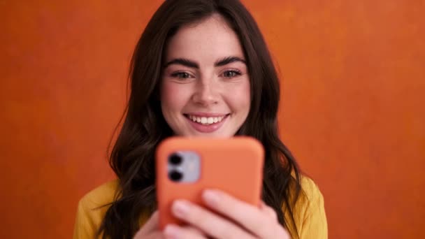 Een Mooie Jonge Vrouw Gebruikt Haar Smartphone Geïsoleerd Een Oranje — Stockvideo