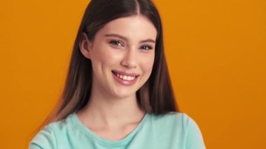 Mutlu genç bir kadın stüdyoda turuncu arka planda dikilip duruyor.