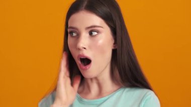 Şaşırmış genç bir kadın, stüdyoda turuncu arka planda tek başına dururken ağzını açıyor.
