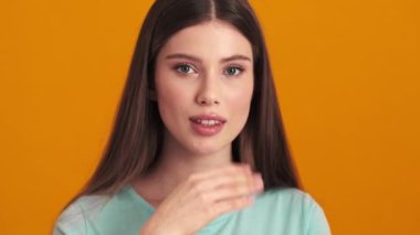 Güzel genç bir kadın, stüdyoda turuncu arka planda duran bir öpücük yolluyor.